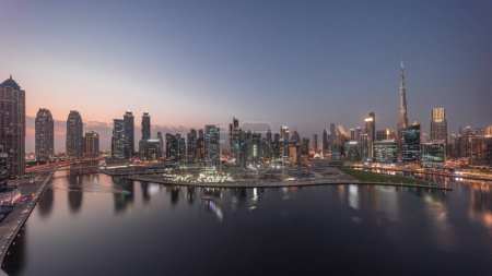 Téléchargez les photos : Panorama aérien de Dubai Business Bay et du centre-ville avec les différents gratte-ciel et tours le long du front de mer sur le canal de jour comme de nuit passage timelapse. Site de construction avec grues après le coucher du soleil - en image libre de droit
