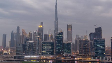 Photo for Aerial view to Dubai Business Bay and Downtown with the various skyscrapers and towers along waterfront on canal day to night transition timelapse. Construction site with cranes after sunset. Cloudy - Royalty Free Image