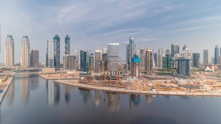 Téléchargez les photos : Paysage urbain avec les gratte-ciel de Dubai Business Bay et le canal d'eau timelapse aérien. Skyline moderne avec des tours résidentielles et de bureaux sur le front de mer. Grand chantier de construction. Nuages sur un ciel bleu - en image libre de droit