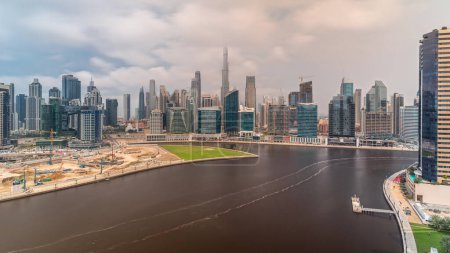 Téléchargez les photos : Vue panoramique aérienne sur Dubai Business Bay et le centre-ville avec les différents gratte-ciel et tours le long du front de mer sur le canal timelapse pendant toute la journée. Site de construction avec grues. Ciel nuageux - en image libre de droit