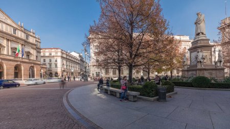 Téléchargez les photos : Panorama montrant le théâtre La Scala timelapse et un petit parc en face du bâtiment historique avec un monument à Léonard de Vinci et ses étudiants. Les gens marchent et s'assoient sur un banc - en image libre de droit