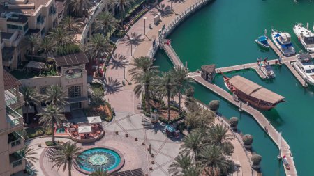 Foto de Dubai Marina waterfront with promenade with fountain aerial timelapse, Dubai, EAU. Muchos restaurantes y yates flotantes y barcos. Las sombras se mueven rápido - Imagen libre de derechos