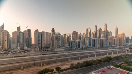 Photo for Panorama of Dubai marina tallest block of skyscrapers timelapse during all day. Aerial view from JLT district to apartment buildings, hotels and office towers near highway with shadows moving fast - Royalty Free Image