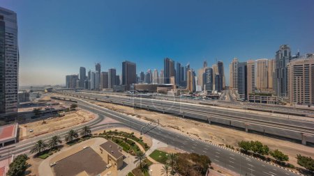 Téléchargez les photos : Dubai Marina gratte-ciel et Sheikh Zayed route avec métro ferroviaire aérien timelapse panoramique pendant toute la journée. Trafic sur une autoroute près de tours modernes avec des ombres se déplaçant rapidement, Émirats arabes unis - en image libre de droit