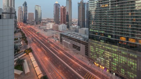 Foto de Barrio de la bahía de negocios skyline arquitectura moderna noche a día timelapse transición desde arriba. Panorama aéreo de los rascacielos y torres de Dubai cerca de la carretera principal antes del amanecer. Tráfico en encrucijada - Imagen libre de derechos