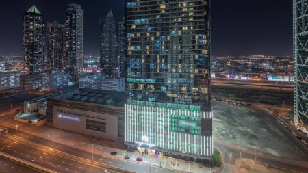 Foto de Panorama que muestra el horizonte del distrito de la bahía de negocios con la noche timelapse de arquitectura moderna desde arriba. Vista aérea de los rascacielos y torres iluminadas de Dubái cerca de la carretera principal. Tráfico en una encrucijada - Imagen libre de derechos