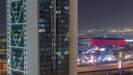 Téléchargez les photos : Vue aérienne vers Dubai City Walk district derrière gratte-ciel la nuit timelapse. Nouvelle partie moderne avec arène, bâtiments de faible hauteur et villas créées comme rues de style européen. Fenêtres éclatantes de tour moderne - en image libre de droit
