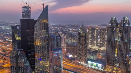 Téléchargez les photos : Bâtiments de grande hauteur sur Sheikh Zayed Road à Dubaï passage aérien du jour à la nuit timelapse, EAU. gratte-ciel dans le quartier financier international d'en haut. Maisons de promenade en ville et villas sur un fond - en image libre de droit