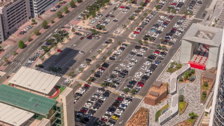 Téléchargez les photos : Vue aérienne de nombreuses voitures colorées stationnées sur le parking avec des lignes et des marquages pour les places de stationnement et les directions timelapse pendant toute la journée. Ombres longues se déplaçant rapidement. Dubai centre financier - en image libre de droit