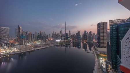 Téléchargez les photos : Panorama aérien de Dubai Business Bay et du centre-ville avec les différents gratte-ciels et tours le long du front de mer sur le canal nuit à jour passage timelapse. Site de construction avec grues avant le lever du soleil - en image libre de droit