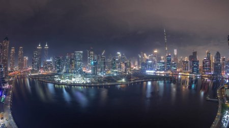 Téléchargez les photos : Panorama aérien de Dubai Business Bay et du centre-ville avec les différents gratte-ciel et tours le long du front de mer sur le canal timelapse nocturne. Site de construction avec grues - en image libre de droit