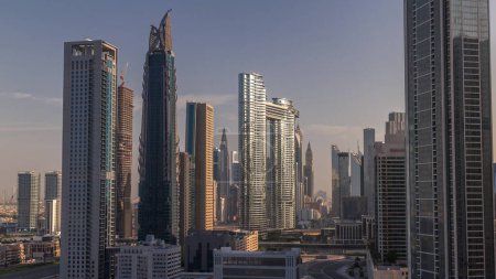 Téléchargez les photos : Tours futuristes et gratte-ciel avec circulation dans les rues de Dubaï Centre-ville et quartier financier. Urbain ville skyline aérienne matin timelapse pendant le lever du soleil. Lumière chaude et soleil réfléchis par le verre - en image libre de droit