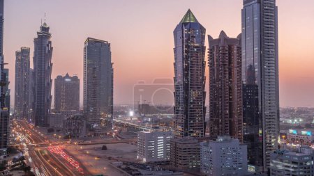 Foto de Skyline distrito de la bahía de negocios con la arquitectura moderna timelapse transición día a noche después de la puesta del sol desde arriba. Vista aérea de los rascacielos y torres de Dubái cerca de la autopista principal. Tráfico en una encrucijada - Imagen libre de derechos