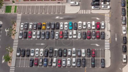 Téléchargez les photos : Vue aérienne de nombreuses voitures colorées stationnées sur le parking avec des lignes et des marquages pour les lieux et les directions pendant toute la journée timelapse avec de longues ombres se déplaçant rapidement. Dubai avenue du quartier financier - en image libre de droit