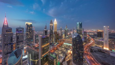 Foto de Vista panorámica del horizonte de los edificios de gran altura en Sheikh Zayed Road en Dubai día aéreo a la noche timelapse transición, Emiratos Árabes Unidos. Rascacielos iluminados en el Centro Financiero Internacional desde arriba - Imagen libre de derechos