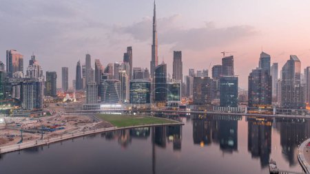 Foto de Vista aérea de Dubai Business Bay y el centro de la ciudad con los diversos rascacielos y torres a lo largo de la costa en el canal noche a día timelapse transición. Lugar de construcción con grúas antes del amanecer - Imagen libre de derechos