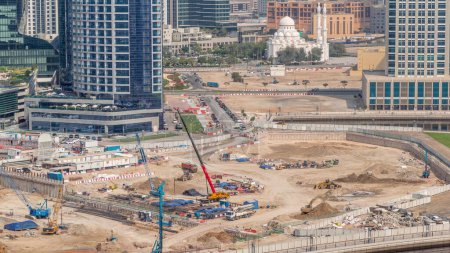 Téléchargez les photos : Pilotage de pieux dans la fosse de fondation pour la construction d'immeubles complexes d'appartements timelapse aérienne. Installation profonde et excavation avec pelles, grues, bulldozers et camions, Dubai Business Bay - en image libre de droit