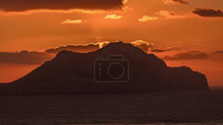 Foto de Puesta de sol en la isla de Amorgos timelapse aéreo desde arriba. Grecia tradicional - cielo naranja sobre montañas y colinas y mar turquesa, Cícladas - Imagen libre de derechos