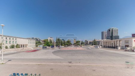 Téléchargez les photos : Panorama montrant la circulation sur le boulevard Deshmoret e Kombit à Tirana timelapse. Rue principale de la capitale albanaise entourée d'arbres verts et de gratte-ciel. Des voitures se déplacent sur la place près de l'université - en image libre de droit
