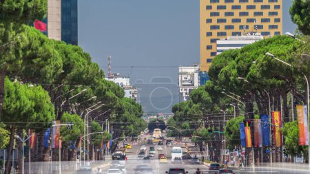 Photo for Traffic on the Deshmoret e Kombit Boulevard in Tirana timelapse. Main street in Albanian capital surrounded by green trees close up view. Cars moving and stops on intersections with a traffic light - Royalty Free Image