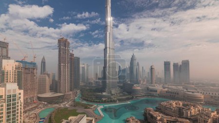 Téléchargez les photos : Vue panoramique aérienne de la ville de Dubaï tôt le matin pendant le timelapse de brouillard. Lever de soleil à horizon futuriste de la ville avec des gratte-ciel et des tours d'en haut. Soleil réfléchi par la surface du verre - en image libre de droit