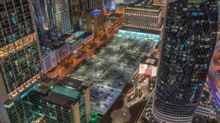 Foto de Vista panorámica del gran estacionamiento rodeado de los edificios de gran altura en Sheikh Zayed Road en Dubai, Emiratos Árabes Unidos. Rascacielos iluminados en el Centro Financiero Internacional desde arriba - Imagen libre de derechos