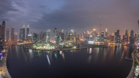 Foto de Vista aérea de Dubai Business Bay y el centro con los rascacielos y torres panorámicos a lo largo de la costa en el canal de día a noche timelapse transición. Lugar de construcción con grúas después del atardecer - Imagen libre de derechos