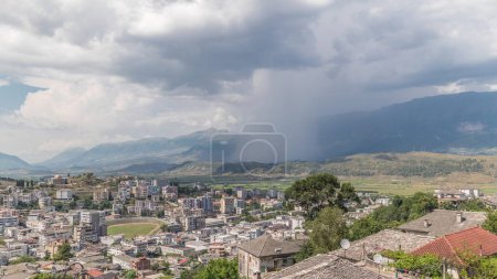 Téléchargez les photos : Panorama montrant la ville de Gjirokastra du point de vue avec de nombreuses maisons historiques typiques avec des toits en pierre de Gjirokaster timelapse. Albanie vue aérienne de la vallée avec nuages de pluie et mouvement de douche - en image libre de droit