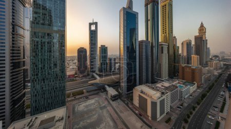 Photo for Aerial panoramic view of Dubai International Financial District with many skyscrapers timelapse during all day. Traffic on a road near multi storey parking with shadows moving fast. Dubai, UAE. - Royalty Free Image