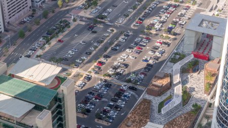 Téléchargez les photos : Vue aérienne de nombreuses voitures colorées stationnées sur le parking avec des lignes et des marquages pour les places de stationnement et les directions timelapse pendant toute la journée. Ombres longues se déplaçant rapidement. Dubai centre financier - en image libre de droit