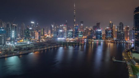 Photo for Aerial panoramic view to Dubai Business Bay and Downtown with various skyscrapers and towers along waterfront on canal night timelapse during all night. Construction site with cranes. Blinking lights - Royalty Free Image
