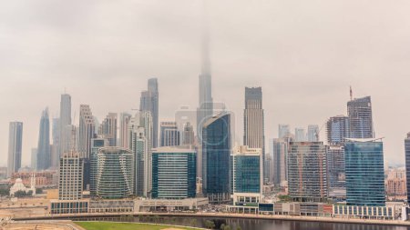 Foto de Vista aérea de Dubai Business Bay y el centro de la ciudad con los diversos rascacielos y torres a lo largo de la costa en el timelapse canal. Planta de construcción con grúas. Cielo nublado durante todo el día - Imagen libre de derechos