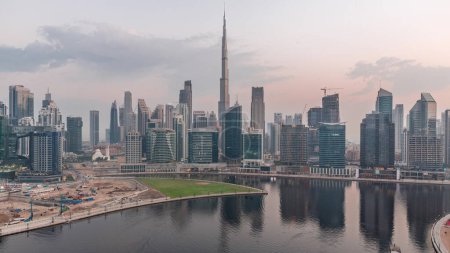 Téléchargez les photos : Vue aérienne vers Dubai Business Bay et le centre-ville avec les différents gratte-ciels et tours le long du front de mer sur le canal nuit à jour passage timelapse. Site de construction avec grues avant le lever du soleil - en image libre de droit