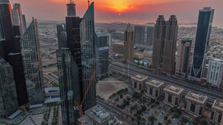 Foto de Edificios de gran altura en Sheikh Zayed Road en Dubai, Emiratos Árabes Unidos. Rascacielos en el distrito financiero internacional desde arriba durante la puesta del sol. Paseo por la ciudad casas y villas en el fondo. Cielo naranja - Imagen libre de derechos
