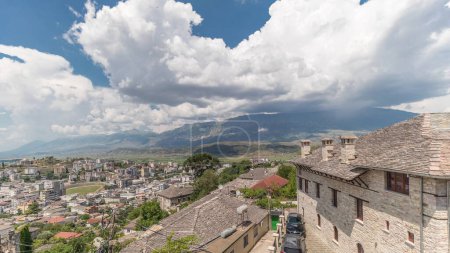 Foto de Panorama que muestra la ciudad de Gjirokastra desde el mirador con muchas casas históricas típicas con techos de piedra de Gjirokaster timelapse. Albania vista aérea al valle con nubes en un cielo azul - Imagen libre de derechos