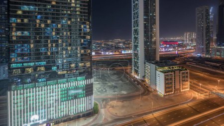 Foto de Panorama que muestra el horizonte del distrito de la bahía de negocios con la noche timelapse de arquitectura moderna desde arriba. Vista aérea de los rascacielos y torres iluminadas de Dubái cerca de la carretera principal. Tráfico en una encrucijada - Imagen libre de derechos