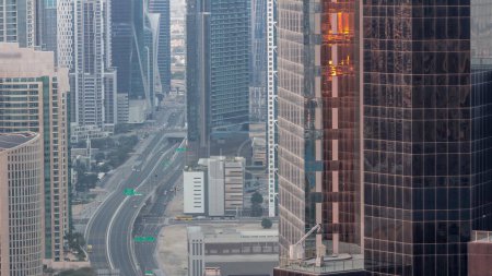 Foto de Vista aérea desde arriba a concurridas intersecciones en Dubai noche a día timelapse transición. Coches que conducen directamente hacia adelante en ambas direcciones de la carretera antes del amanecer. Rascacielos del distrito de negocios - Imagen libre de derechos