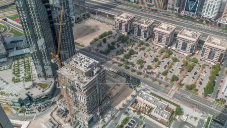 Foto de Sitio de construcción con grúas y edificios en Sheikh Zayed Road en Dubai, Emiratos Árabes Unidos. Rascacielos en el distrito financiero desde arriba con largas sombras en movimiento. Estacionamiento con muchos coches - Imagen libre de derechos