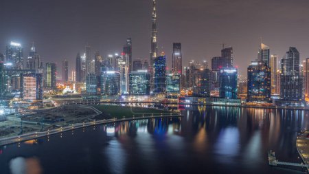 Foto de Vista aérea a Dubai Business Bay y el centro de la ciudad durante toda la noche con los diversos rascacielos y torres a lo largo de la costa en la noche del canal timelapse. Construcción con grúas - Imagen libre de derechos