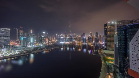 Photo for Aerial view to Dubai Business Bay and Downtown with the various skyscrapers and towers covered by fog during all night. Waterfront and canal night timelapse. Construction site with cranes - Royalty Free Image