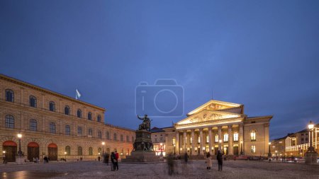 Foto de Teatro Nacional de Múnich o Teatro Nacional en la plaza Max Joseph día a noche timelapse transición. Histórico teatro de ópera, sede de la Ópera Estatal de Baviera. La estatua en el centro. Alemania - Imagen libre de derechos