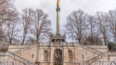 Téléchargez les photos : Vue de face de la célèbre colonne de la Paix avec statue en or de l'Ange de la Paix (Friedensengel) timelapse, les gens et le parc public dans la capitale bavaroise près de la rivière Isar. Allemagne, Munich, Bogenhausen - en image libre de droit