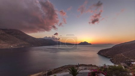 Panorama showing orange clouds during sunset on Amorgos island aerial timelapse from above. Traditional Greece - white houses on hills and turquoise sea, Cyclades