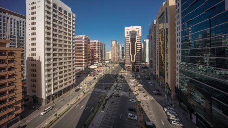 Téléchargez les photos : Bâtiments résidentiels et architecture moderne de la ville d'Abu Dhabi timelapse aérien pendant toute la nuit jusqu'au lever du soleil, Émirats arabes unis. Vue d'en haut pour les voitures sur le parking et de longues ombres des tours avec des gratte-ciel - en image libre de droit