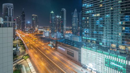 Foto de Skyline distrito de la bahía de negocios con arquitectura moderna timelapse panorámica durante toda la noche desde arriba. Vista aérea de los rascacielos y torres iluminadas de Dubái cerca de la carretera principal. Tráfico en encrucijada - Imagen libre de derechos