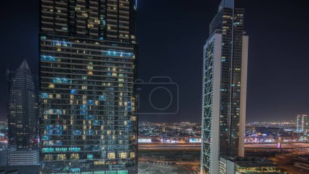Foto de Panorama que muestra la vista aérea del centro de Dubái y el horizonte de la bahía de negocios con muchas torres iluminadas de noche timelapse. Zona de lujo en la ciudad urbana inteligente. Rascacielos y edificios de gran altura desde arriba - Imagen libre de derechos