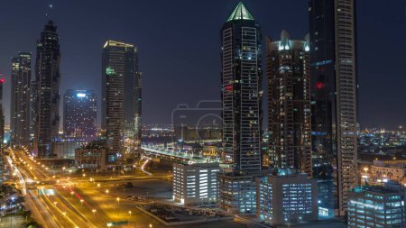 Téléchargez les photos : Business Bay skyline de quartier avec l'architecture moderne timelapse pendant toute la nuit d'en haut. Vue aérienne des gratte-ciel de Dubaï avec des fenêtres clignotantes et des tours éclairées près de la circulation routière principale - en image libre de droit