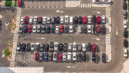 Téléchargez les photos : Vue aérienne de nombreuses voitures colorées stationnées sur le parking avec des lignes et des marquages pour les lieux et les directions pendant toute la journée timelapse avec de longues ombres se déplaçant rapidement. Dubai avenue du quartier financier - en image libre de droit