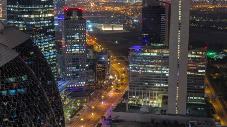 Téléchargez les photos : Vue aérienne des immeubles de grande hauteur sur la route courbée animée de Dubaï pendant toute la nuit timelapse, Émirats arabes unis. Des gratte-ciels de bureaux éclairés dans la place financière internationale d'en haut - en image libre de droit
