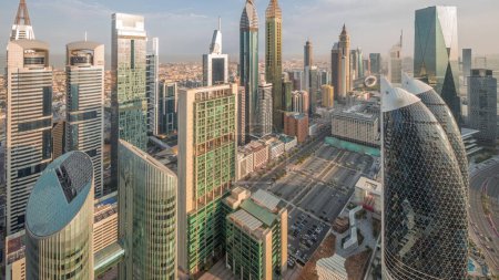Foto de Vista panorámica de edificios de gran altura en Sheikh Zayed Road Dubai aéreo noche a día timelapse transición, Emiratos Árabes Unidos. Rascacielos en el Centro Financiero Internacional desde arriba durante el amanecer con largas sombras - Imagen libre de derechos